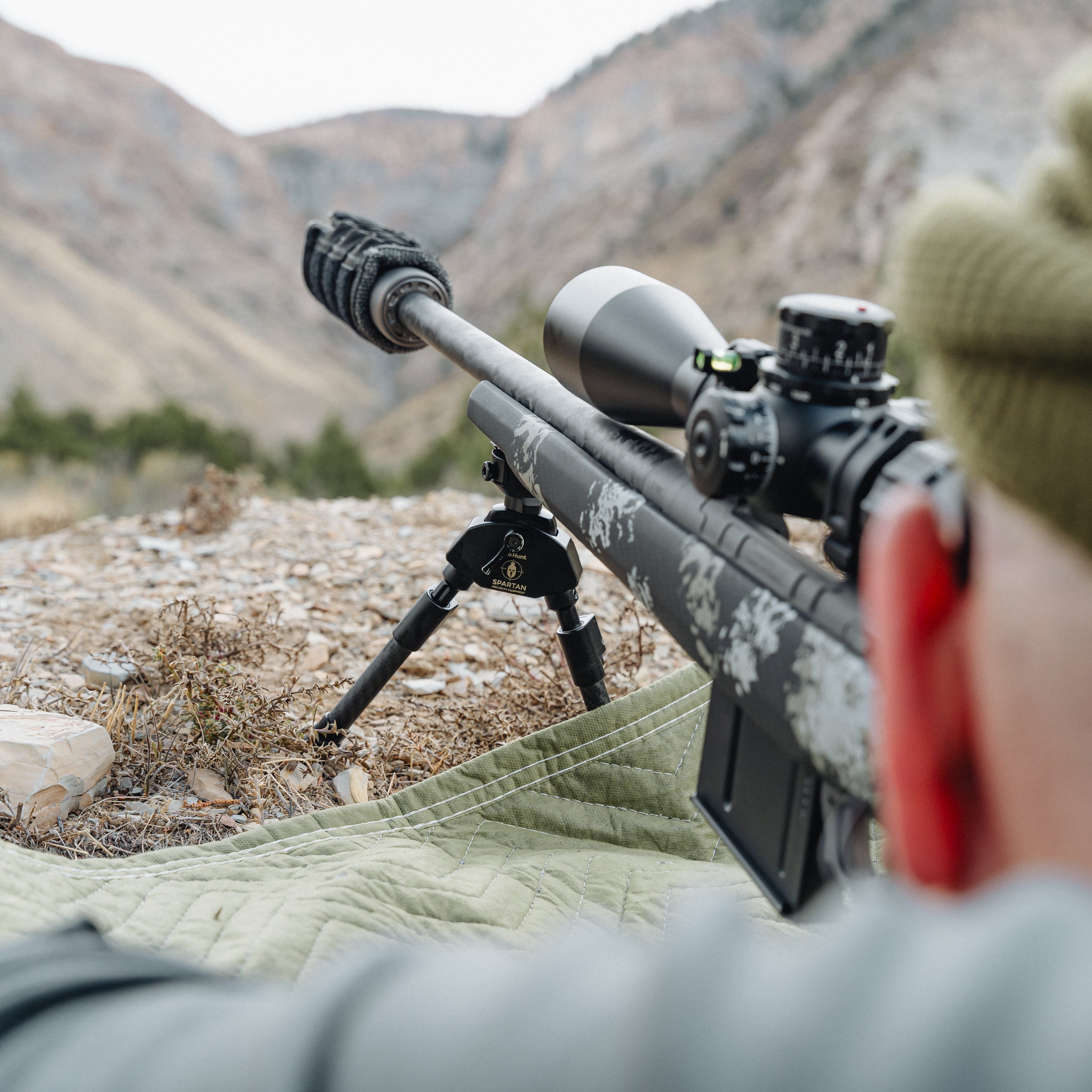 Person with a rifle and scope in a mountainous landscape