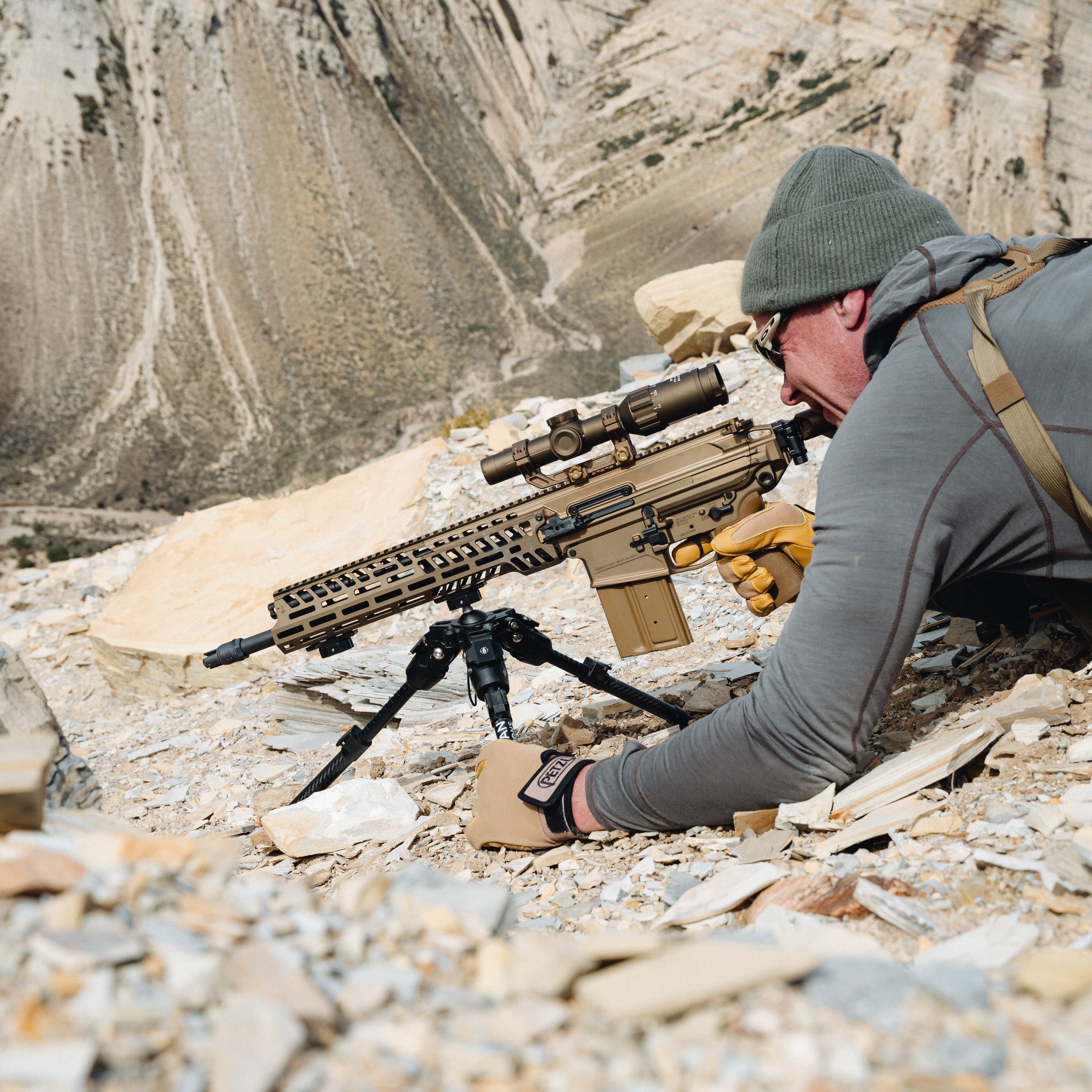 Person in a mountainous area with a rifle on a tripod