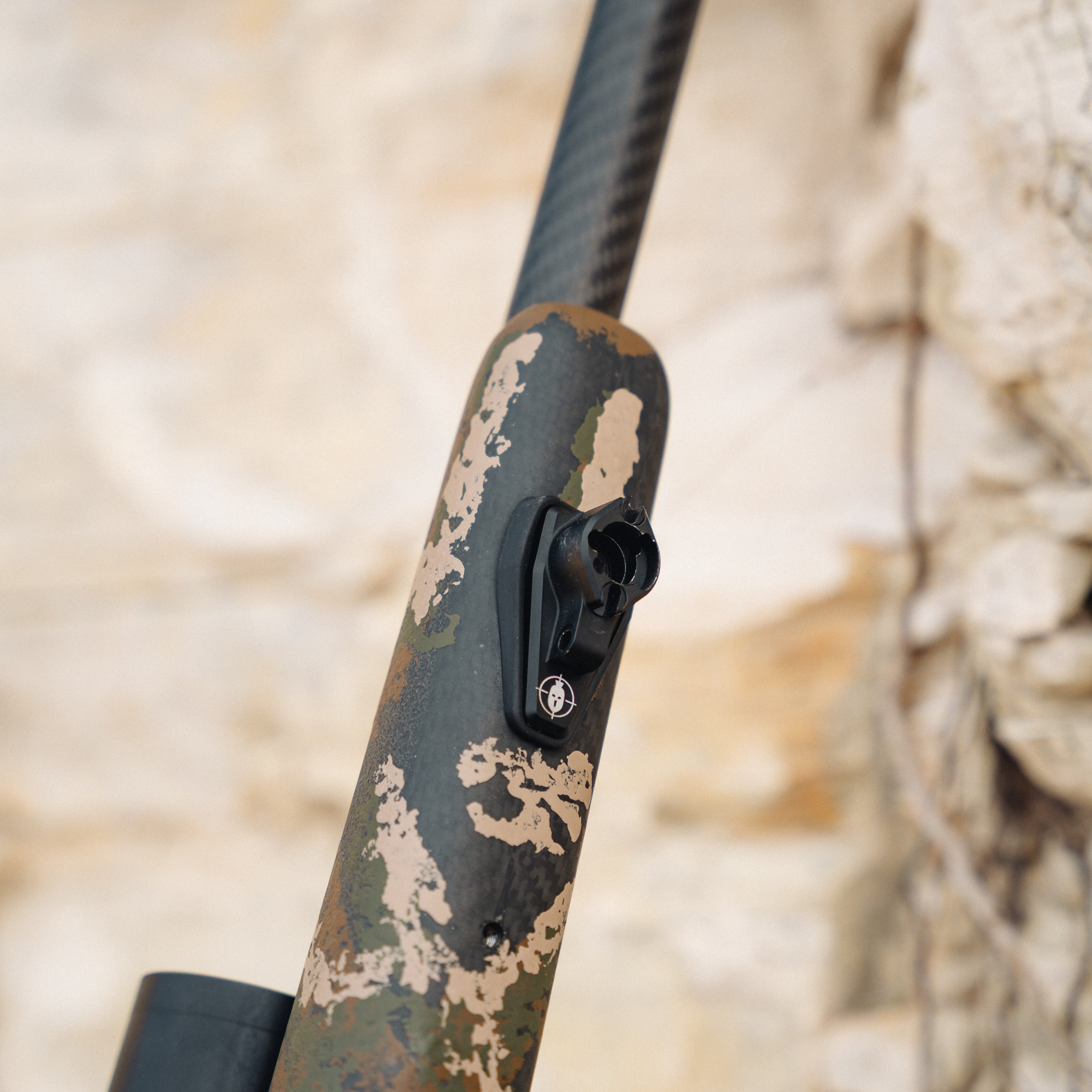 Camouflage-patterned rifle stock with a blurred natural background